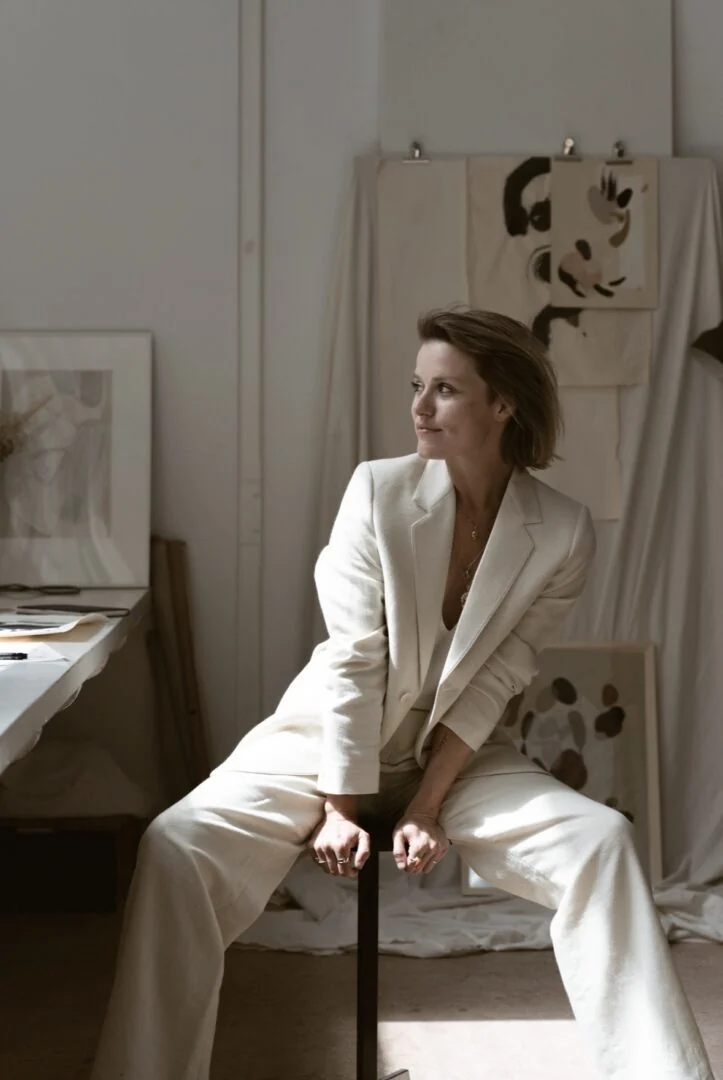 Sella seated in a white suit in an artist's studio.