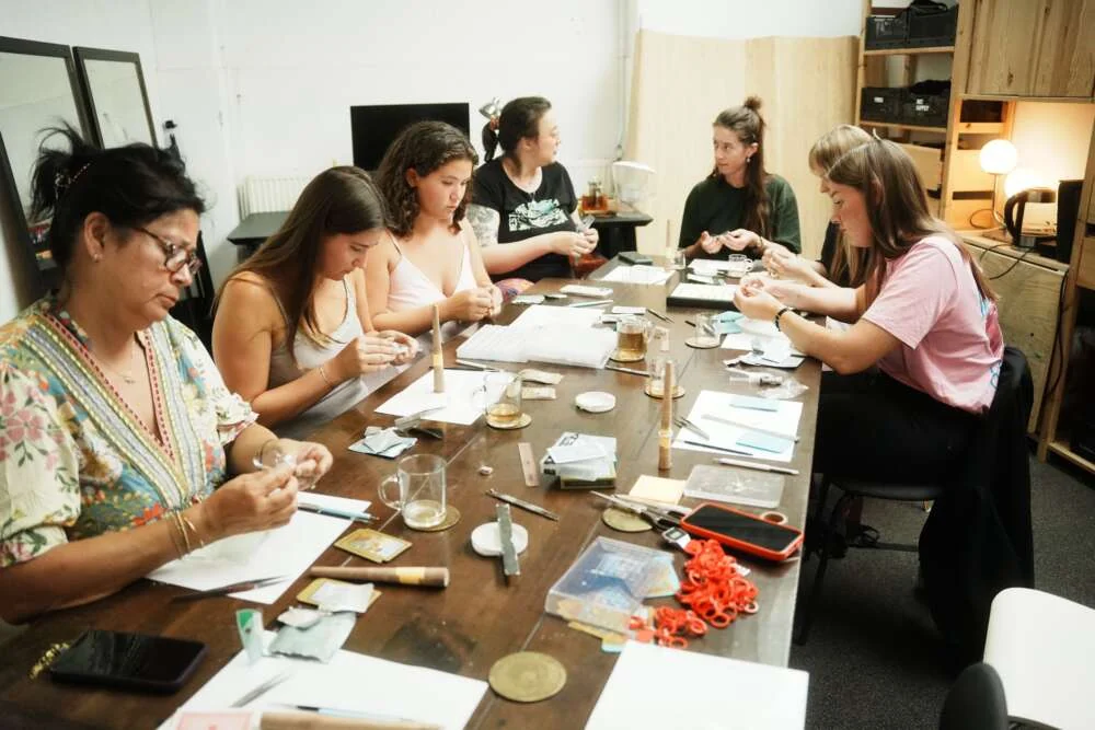 Colleagues round a long workshop table carving wax rings in a bright studio.