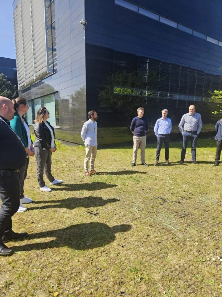 Colleagues standing in a loose circle on the grass outside a dark glass office building.