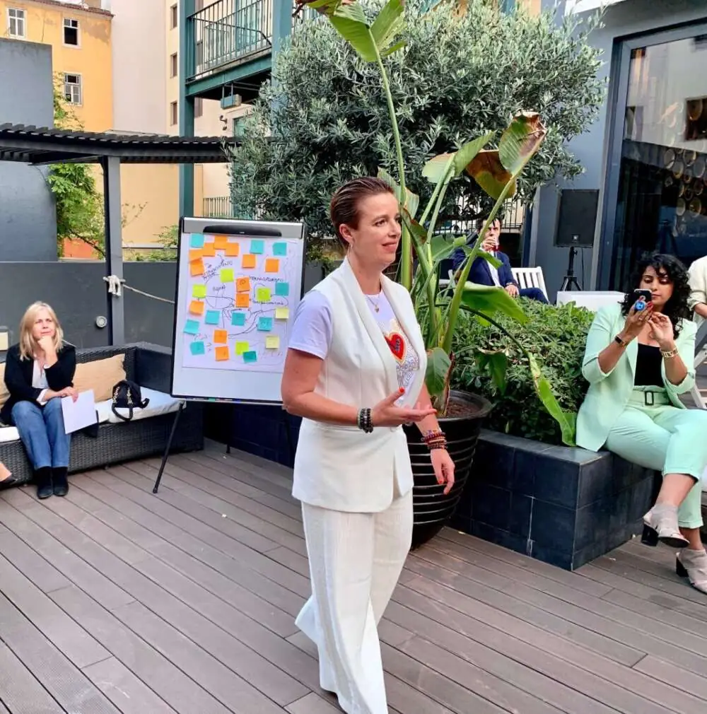 A facilitator speaking to a group on a terrace beside a flip chart