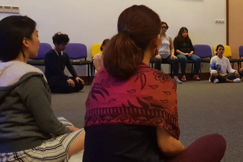 A group seated in a circle on the floor of a meeting room