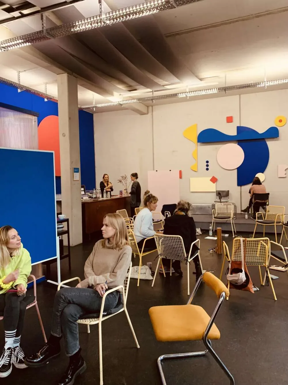 Participants seated on scattered chairs in a colourful workshop space, talking in small groups