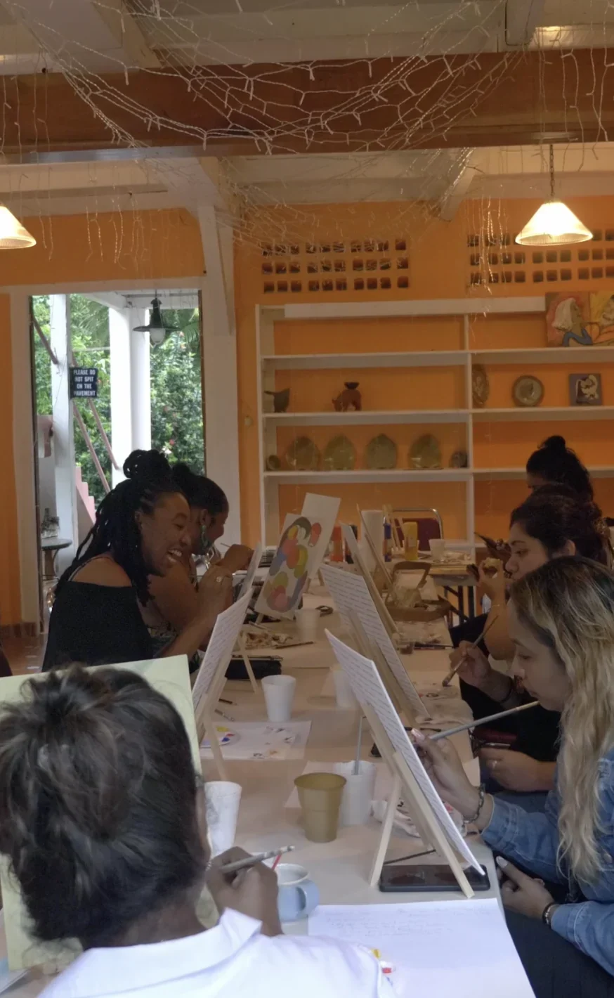 Colleagues painting at long tables in a warm studio, one of them laughing