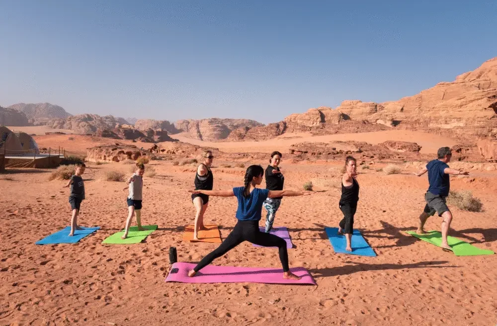 A group holding a warrior pose together on colourful mats in a red desert