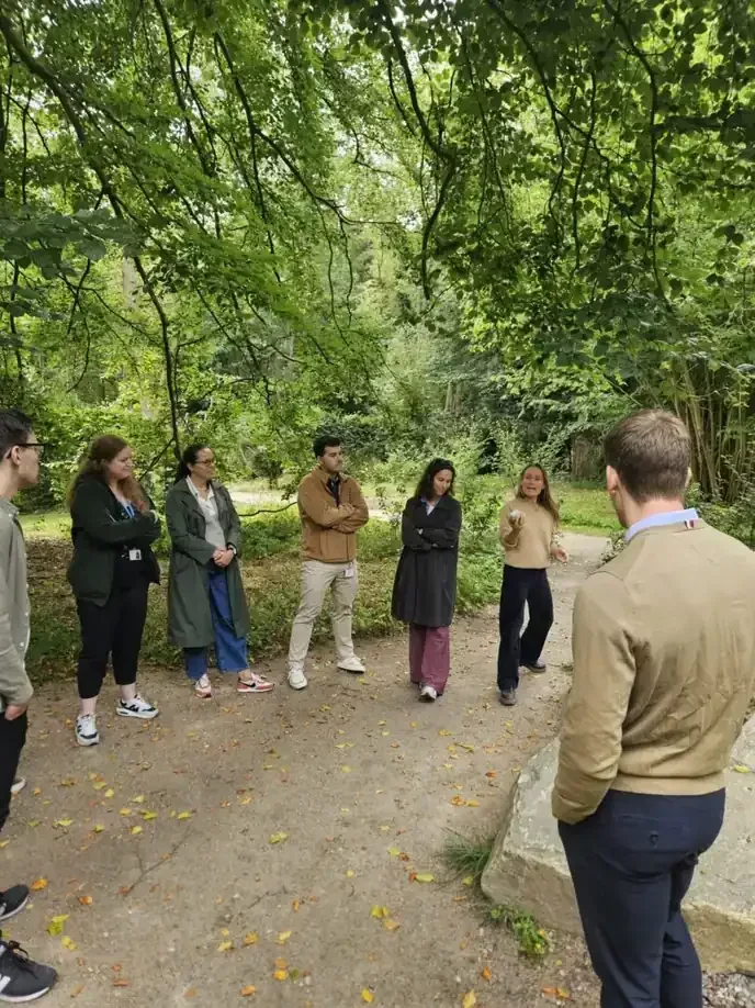 A small group standing in a circle on a forest path, listening to their guide among tall trees