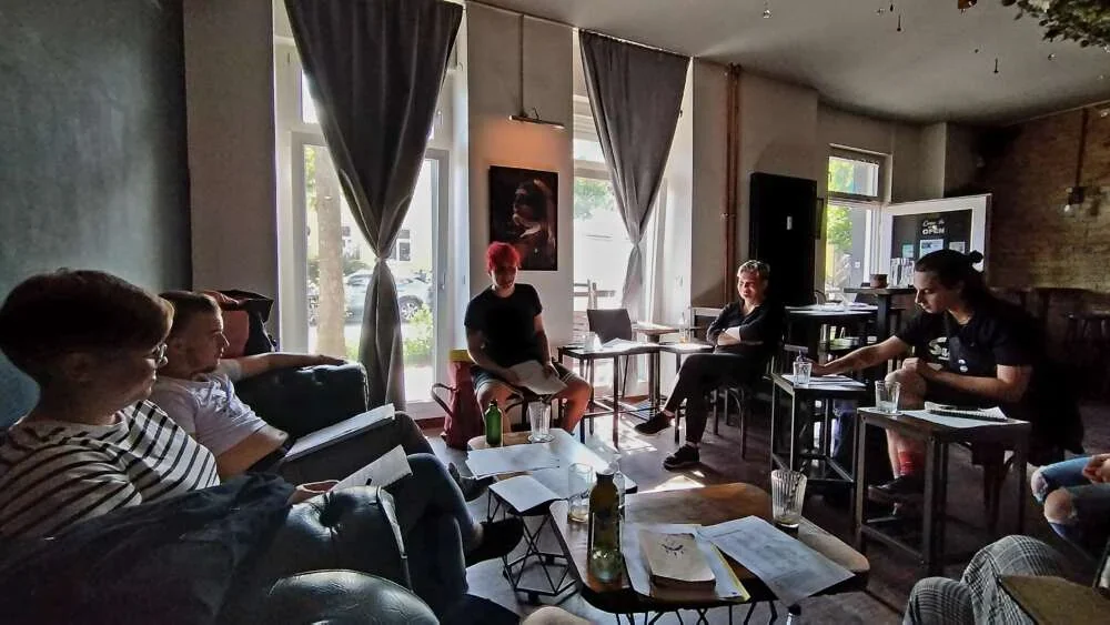 A small group seated around low tables with worksheets during a facilitated conversation in a sunlit room