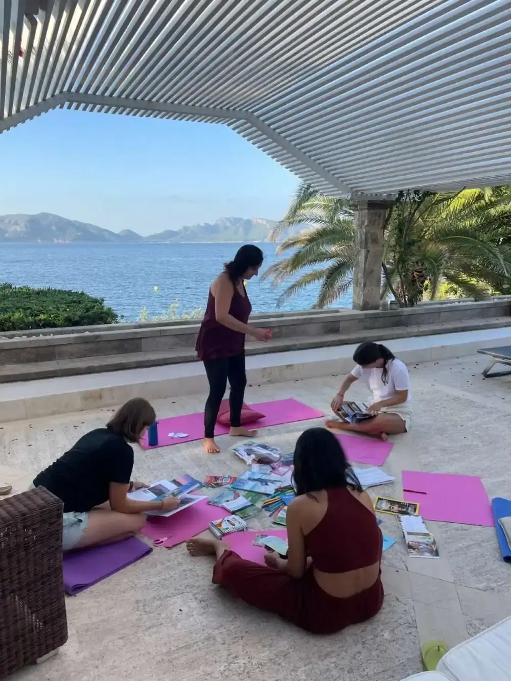 A facilitator moving between participants working on mats on a seaside terrace
