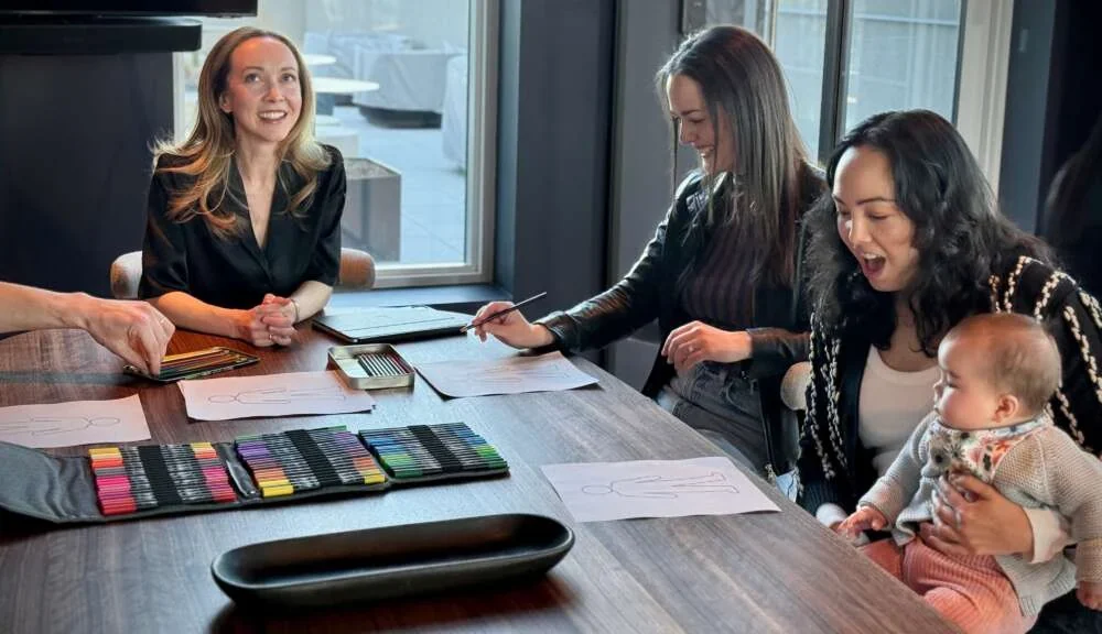 Three women laughing around a meeting table laid with coloured pens during a New York session
