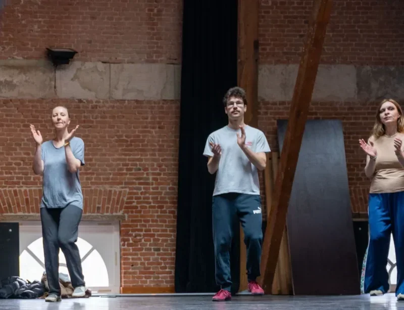 Briana leading colleagues as they clap one rhythm together in a brick-walled hall