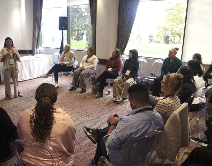 Marcela guiding a seated circle of delegates through breathwork in a hotel meeting room