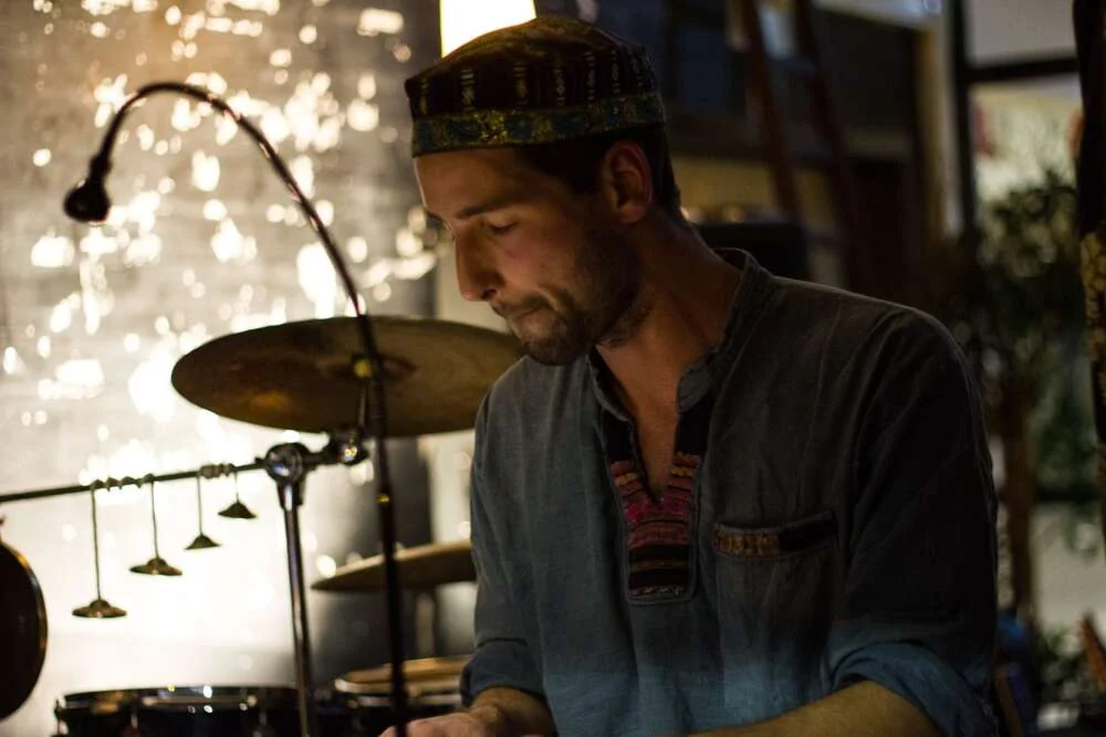 A musician playing drums and percussion on a warmly lit stage