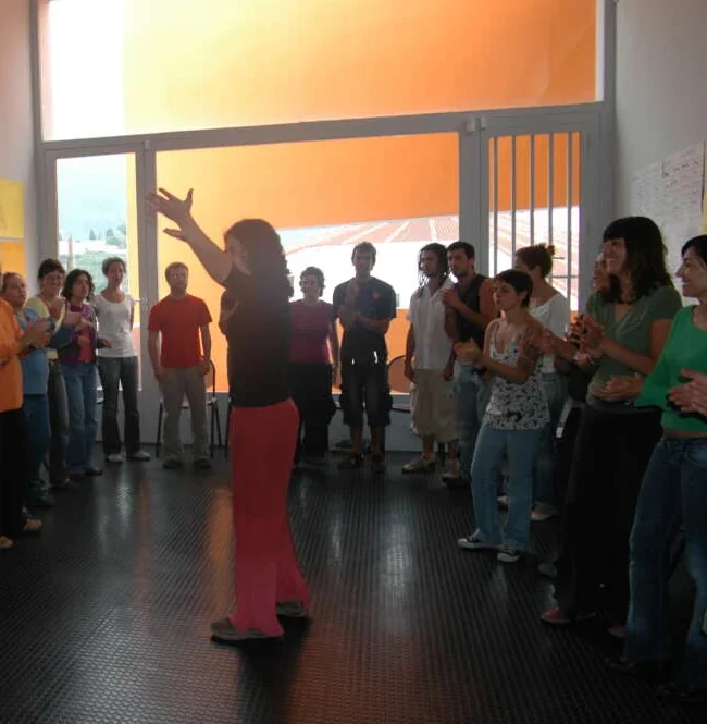 Daniela conducting a standing circle of colleagues as they clap one rhythm together