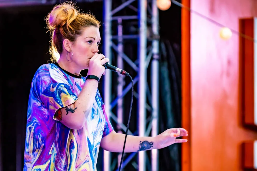 Grace beatboxing into a microphone on a lit stage