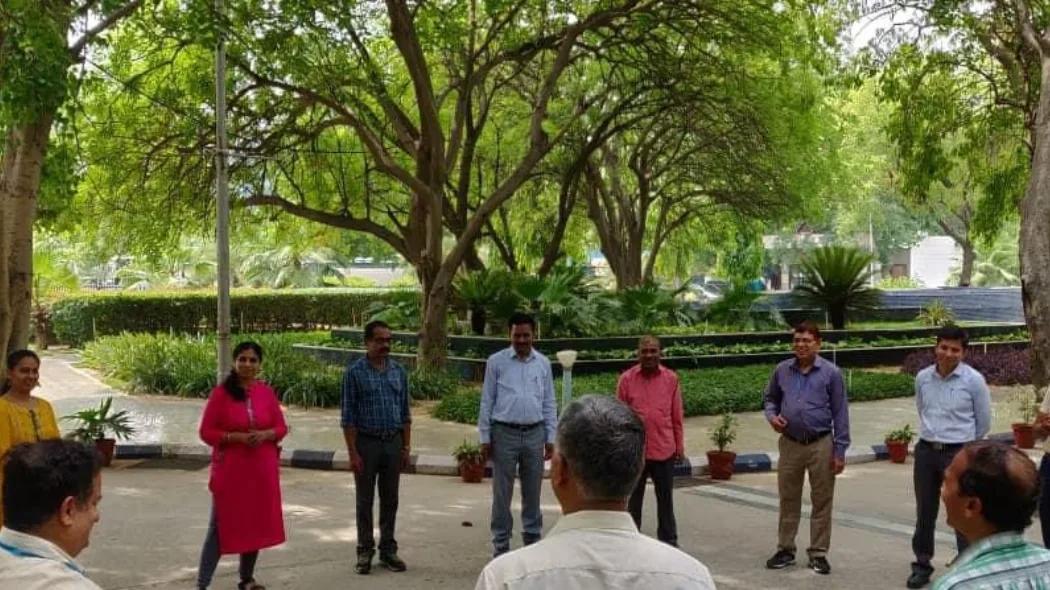 Colleagues standing in a circle under shade trees for an outdoor team exercise