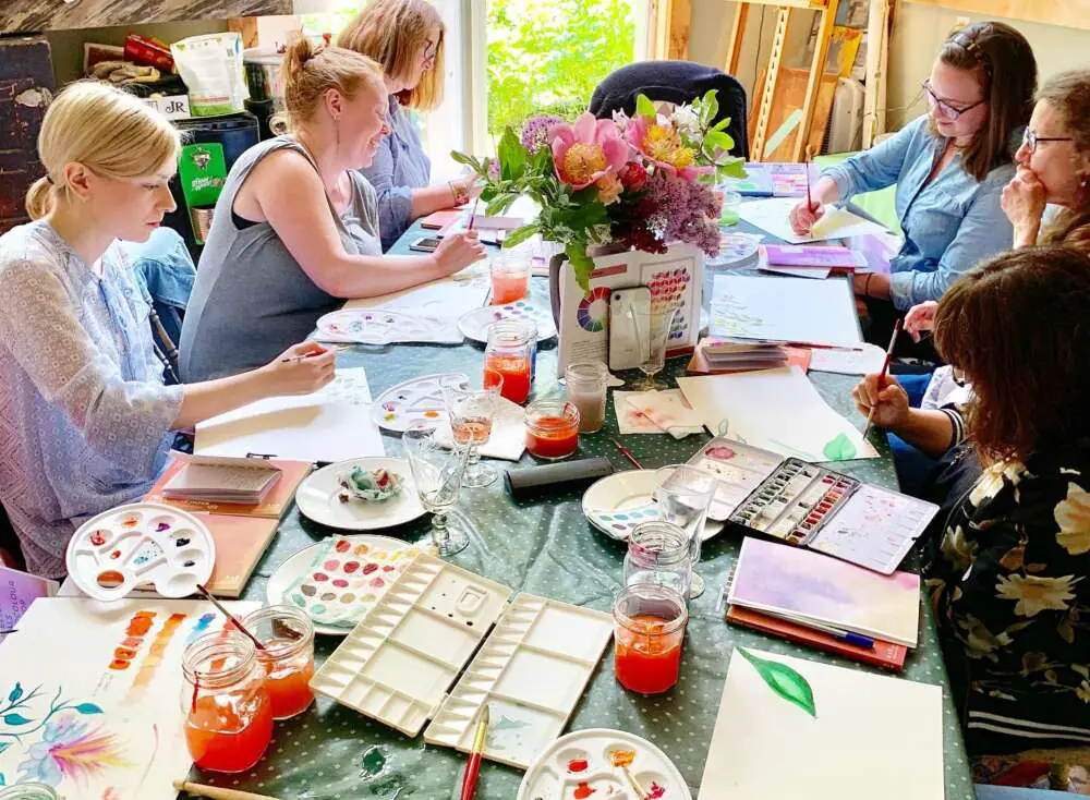 Colleagues painting in watercolour around a table filled with flowers