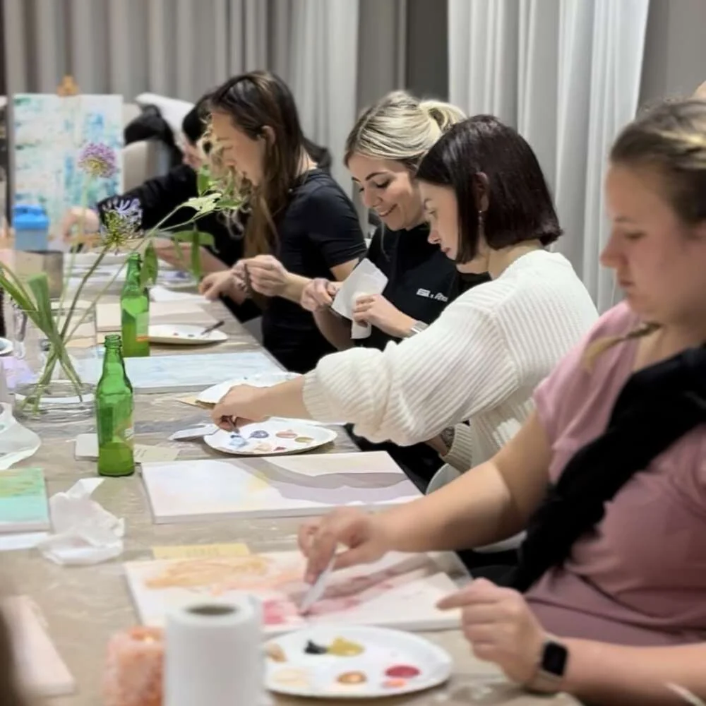 Colleagues painting side by side at a long table during a calm creative workshop