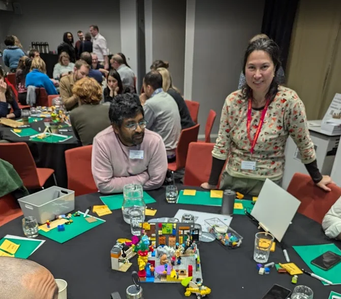 Colleagues build LEGO models around a round table during a facilitated workshop