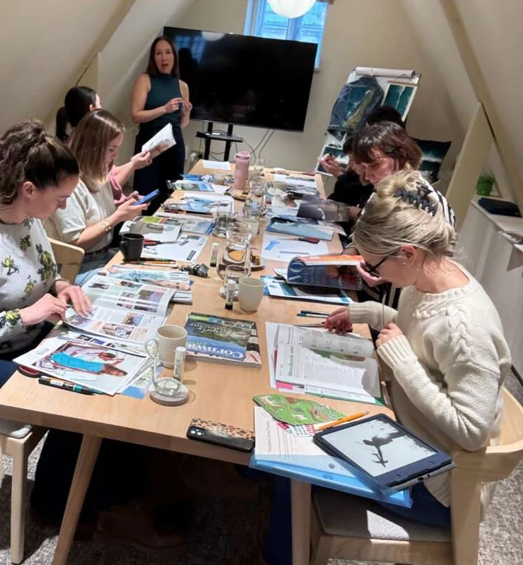 Colleagues making collages at a long table while the host talks them through it