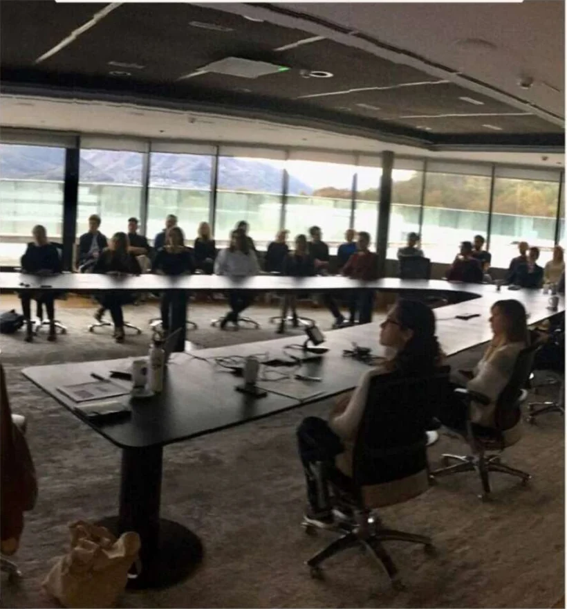 Colleagues listening to a talk round a long table, with windows over the lake and mountains