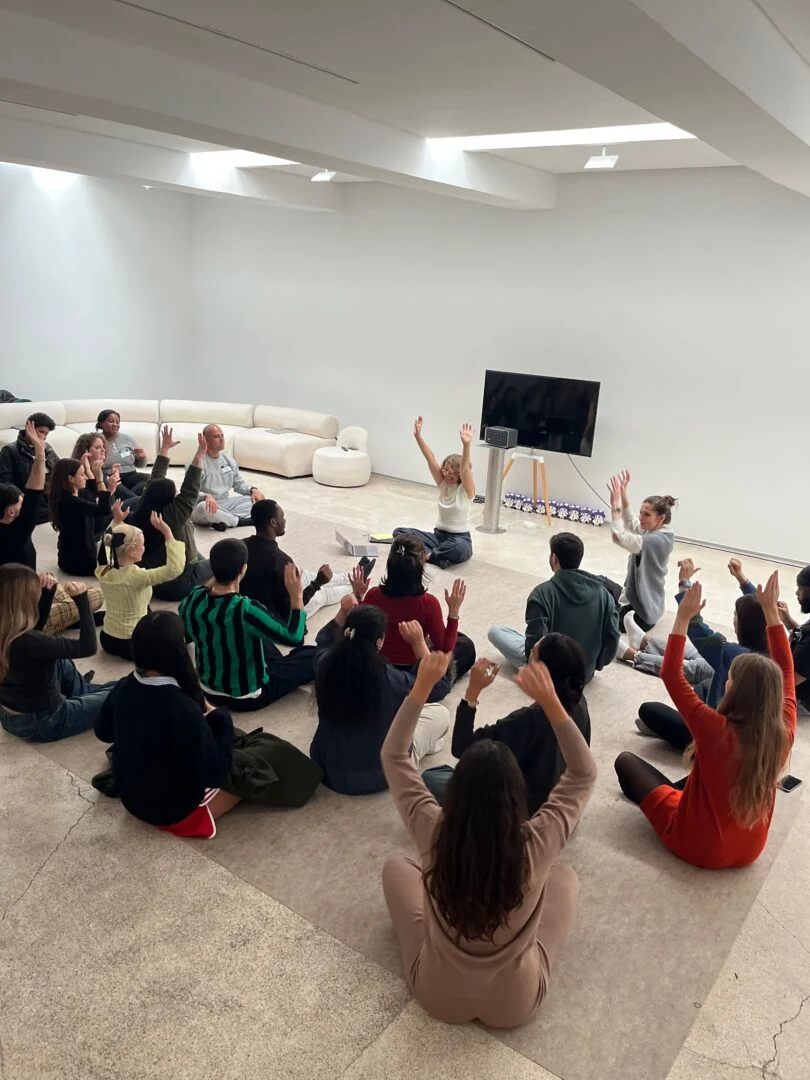 A full hall of colleagues raising their arms together during a movement session