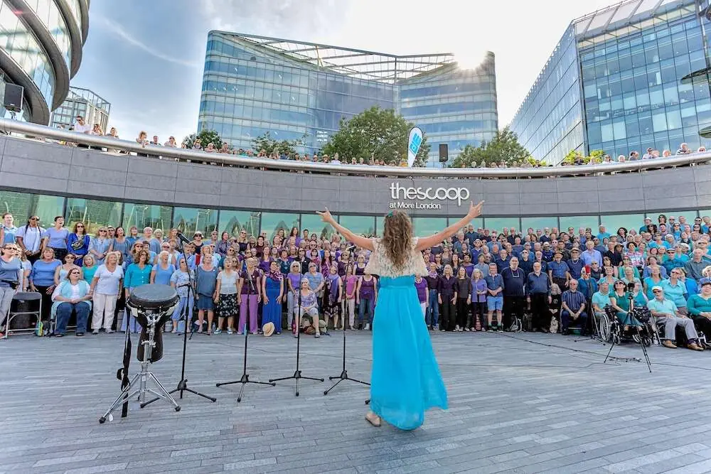 A leader with arms raised before a large group gathered on the riverside amphitheatre by London City Hall