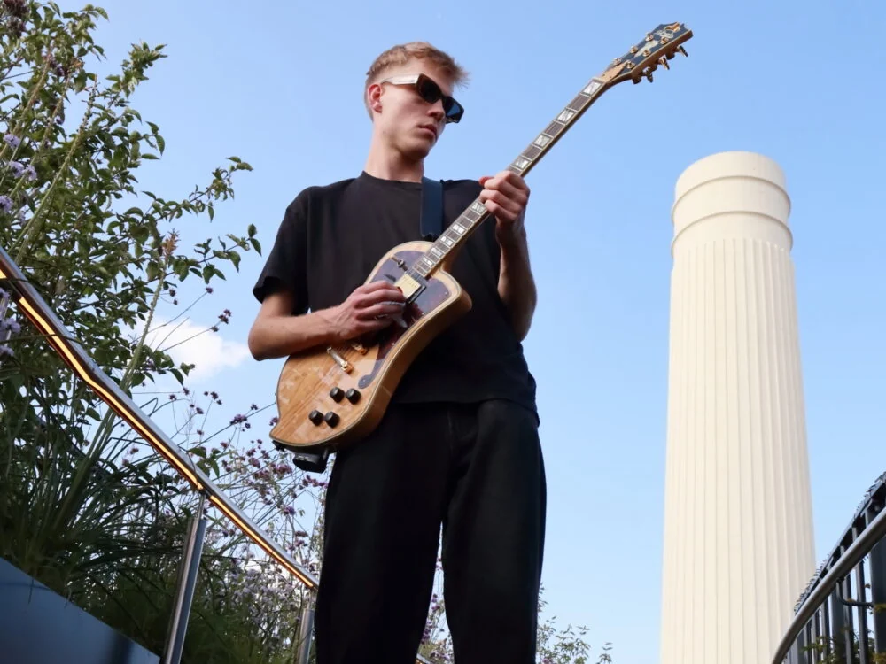 A guitarist playing on a planted rooftop walkway with Battersea Power Station behind