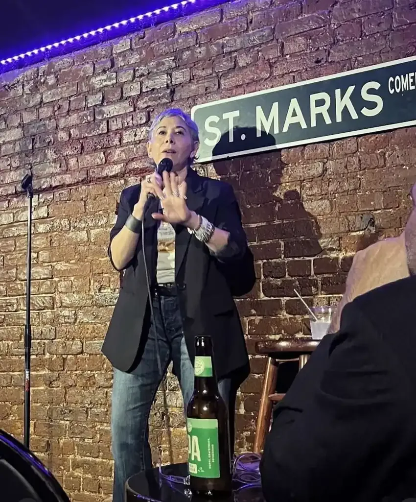 Gina performing stand-up on a brick-walled New York comedy club stage