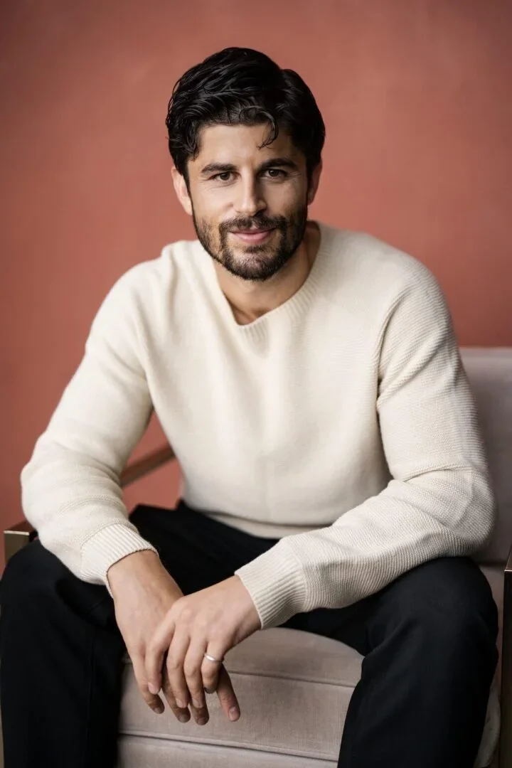 Nick seated in a cream sweater against a terracotta wall