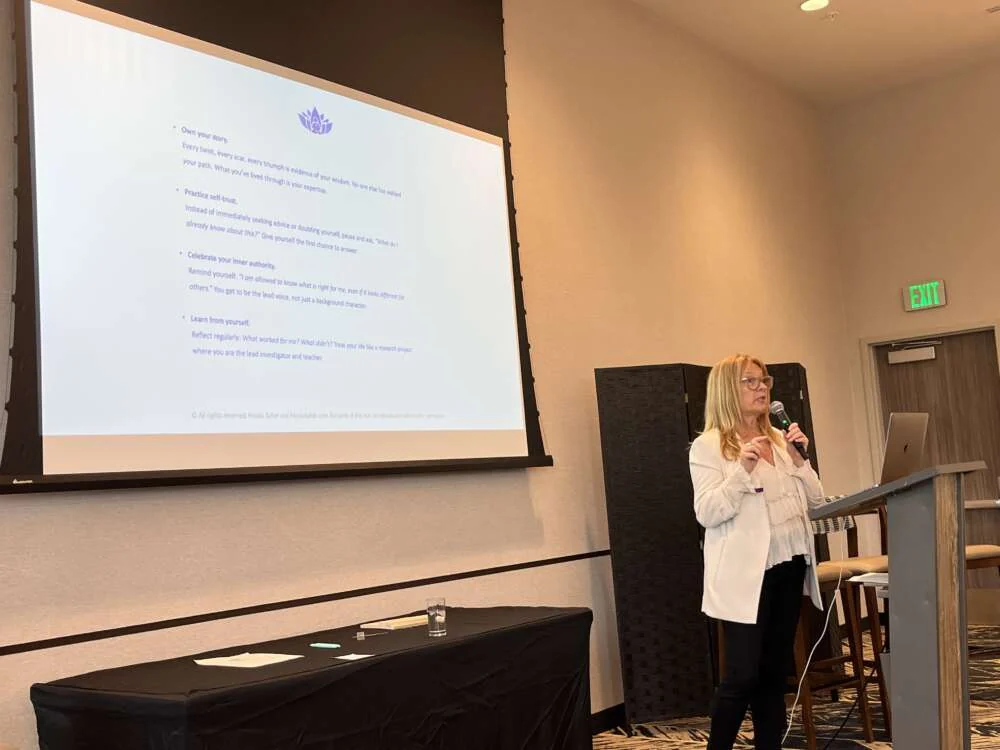 Nicola leading a wellbeing session beside a projected slide in a hotel function room