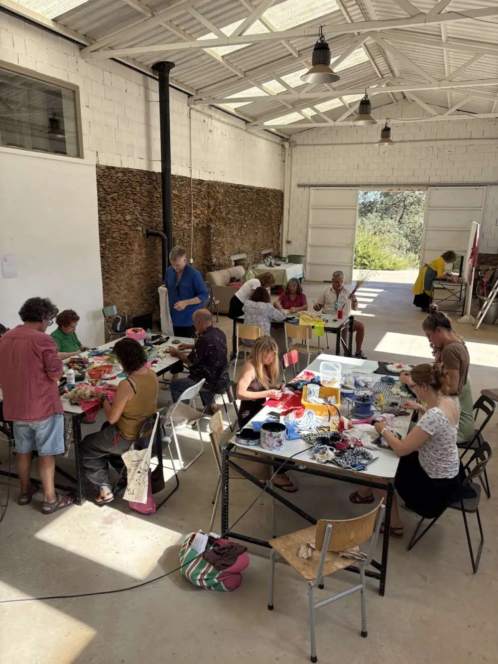 Colleagues sewing and weaving with fabric scraps at tables in a sunlit studio