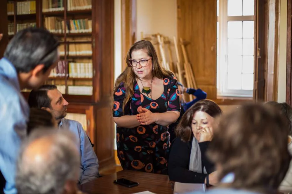 Megan guiding a storytelling game round a table in a wood-panelled library