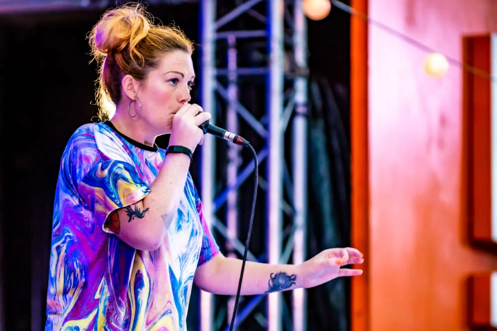 Grace beatboxing into a microphone on a lit stage