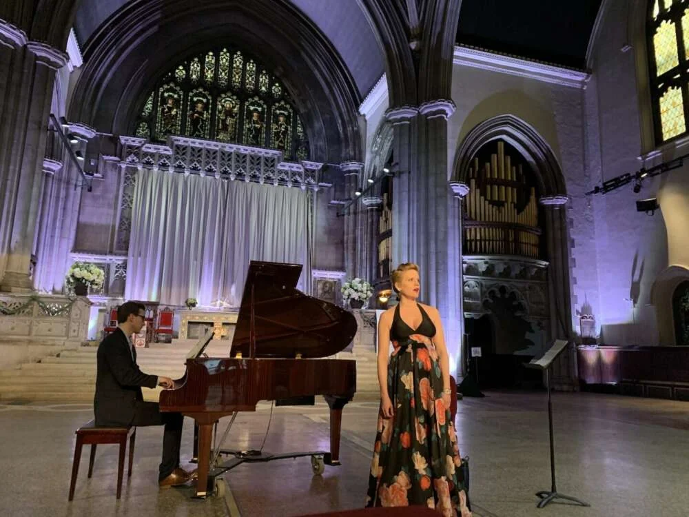 A singer and pianist performing beneath stained glass in a Gothic church hall