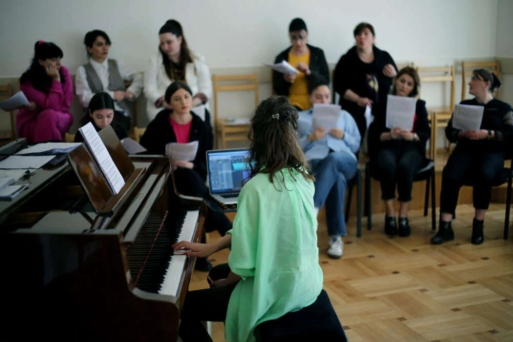 Nuci at the piano leading a choir of colleagues singing from sheet music