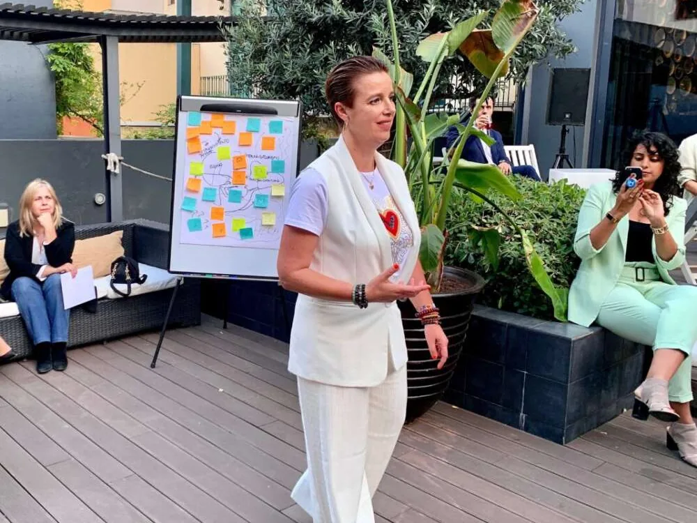 Sandra Isabel leading a writers' room workshop on a rooftop terrace beside a flip chart of sticky notes
