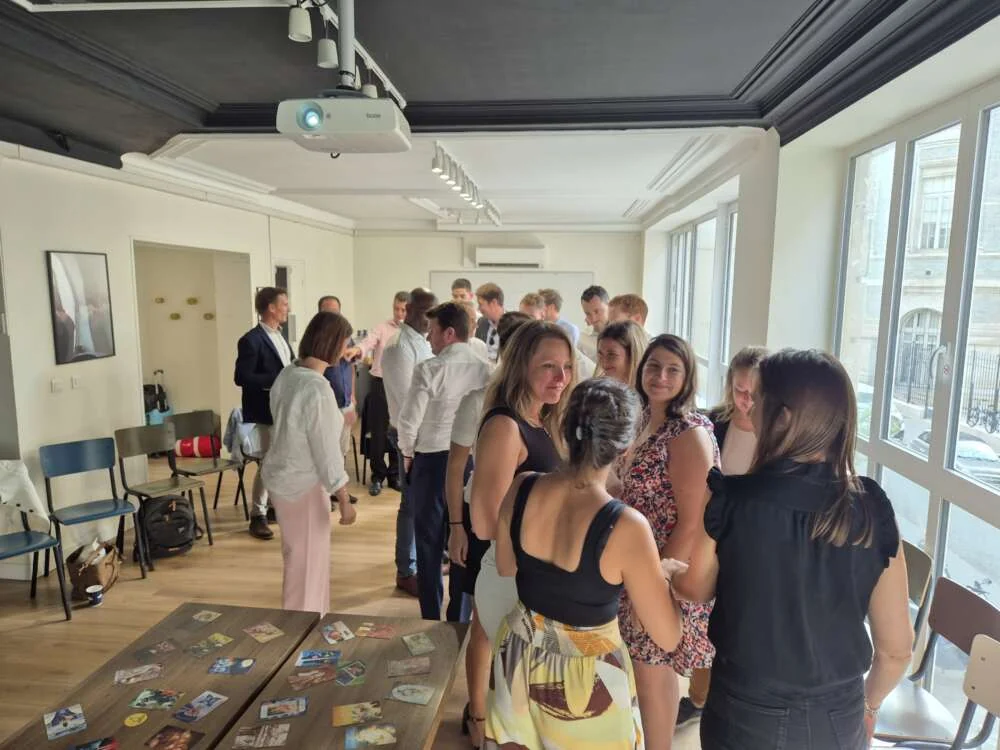 An international team mingling and laughing in a bright Paris meeting room with tall windows