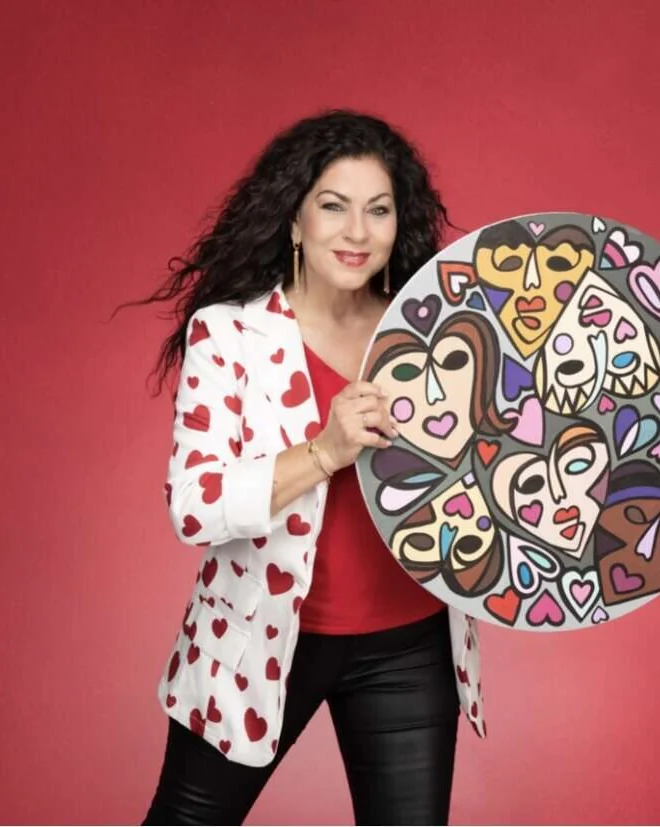 Sherry holding one of her painted artworks against a red wall