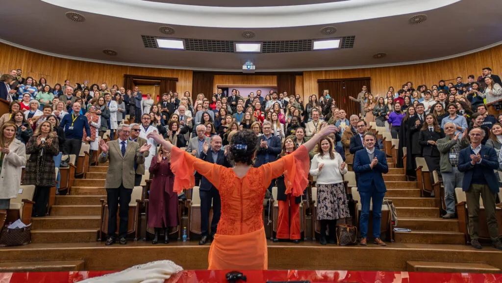 A flamenco dancer in orange facing a full auditorium on its feet, applauding