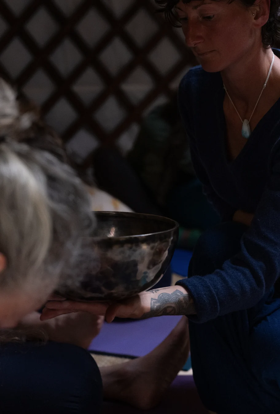 A practitioner holds a singing bowl close to a participant during a sound session in a yurt