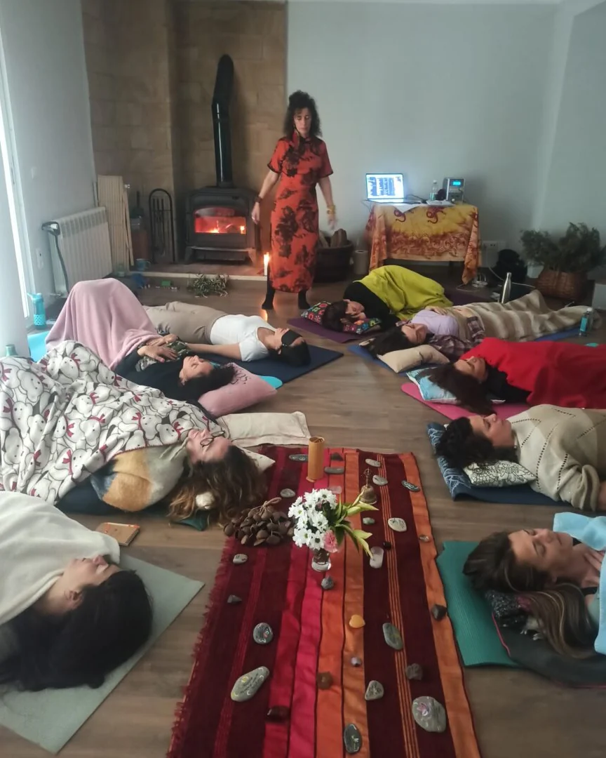 Pilar guiding a group lying on mats beside a wood stove during a breathwork session