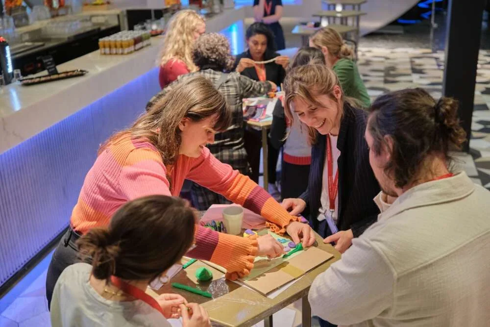 Colleagues laughing as they shape clay at a high table