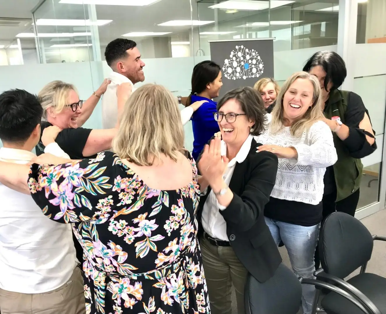Participants laughing as they form a shoulder-to-shoulder chain in a meeting room