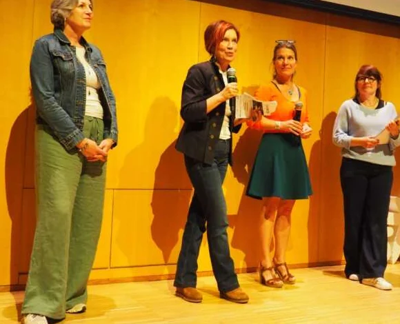 Participants on a wooden stage practising voice work, two of them at microphones