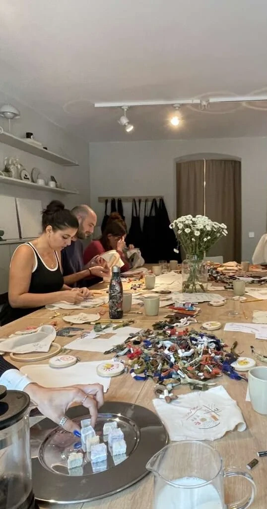 Colleagues embroidering together around a long table set with flowers and thread