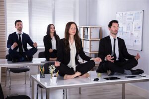 people dressed in suits sitting cross-legged on top of their desks in a meditation pose.