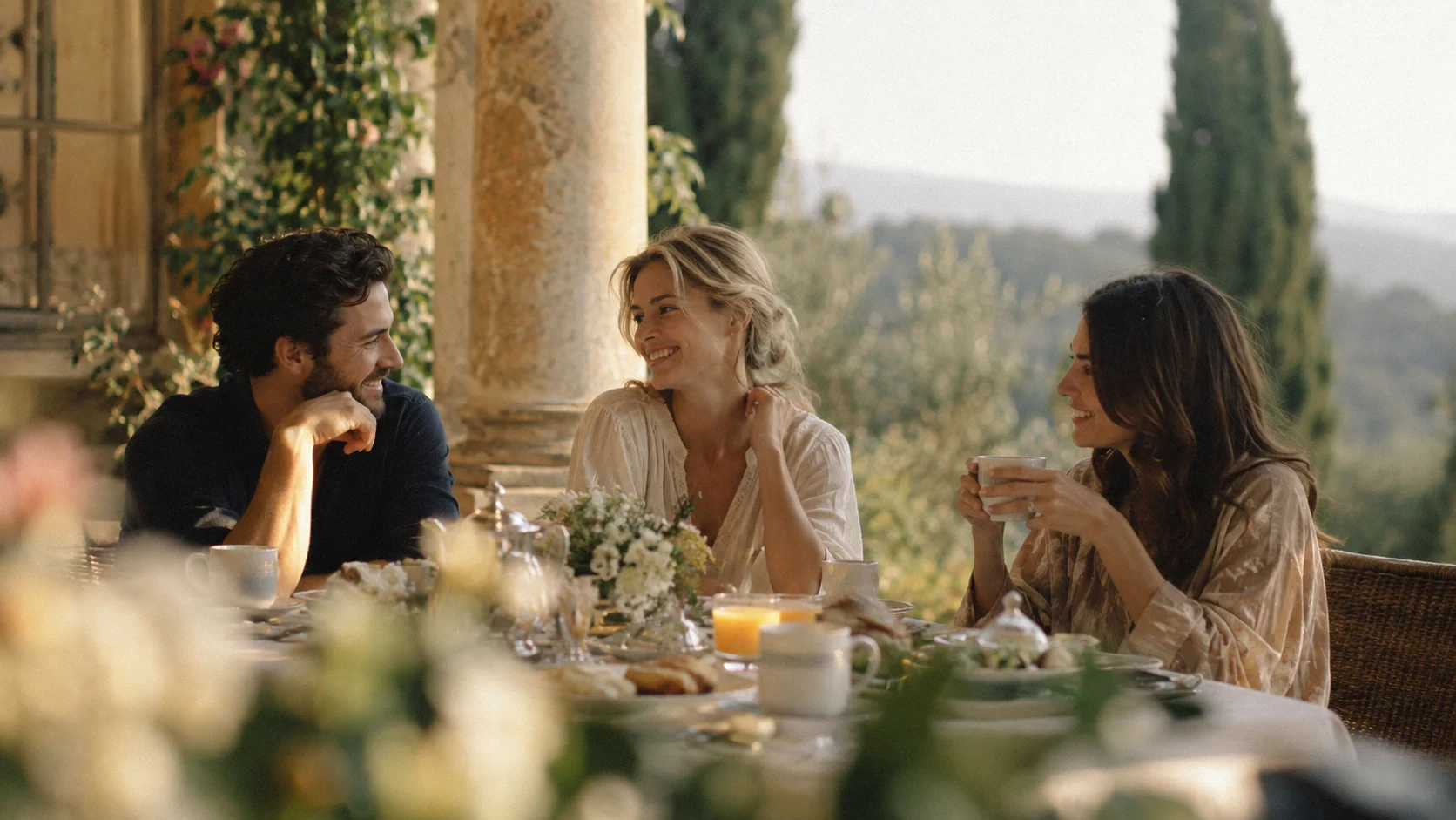 Three friends sharing breakfast on a sunlit terrace overlooking the countryside